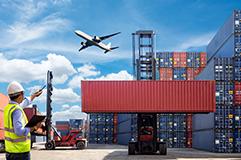 Man pointing toward airplane in the sky that is flying over shipping containers.